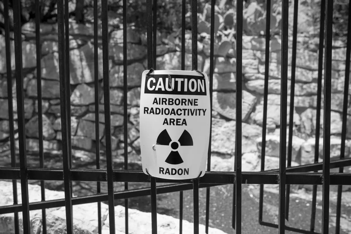A metal caution sign reading Airborne Radioactivity Area, Radon, marked with the radiation trefoil symbol and wired to a fence.